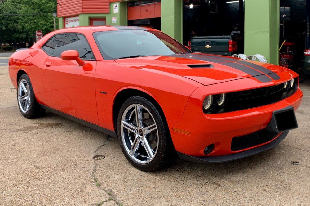 Orange Dodge Challenger with custom wheels in front of the shop