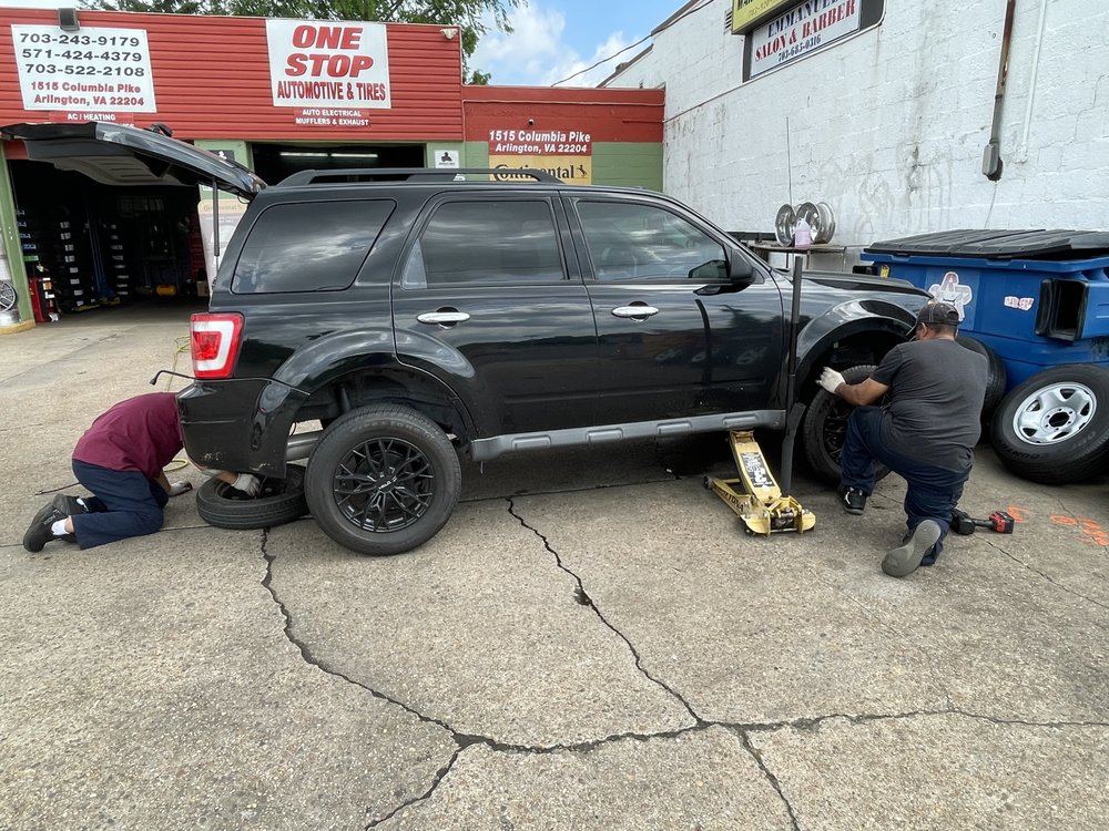 Two technicians fitting wheels on an SUV in front of the One Stop service bays